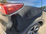 the rear end of a black car with a reflection of a person in the window