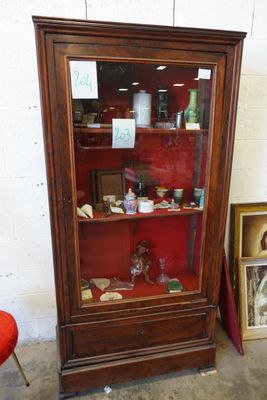 une armoire avec une porte vitrée et une chaise rouge devant