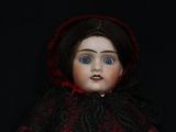 a close up of a doll with blue eyes and a red cape