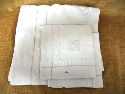 trois draps en lin blanc ornés de motifs brodés, posés sur une table