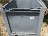un conteneur gris posé par terre à côté d'un tas de tuyaux métalliques