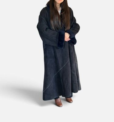 une femme vêtue d'une robe noire et d'un chapeau, debout devant un fond blanc