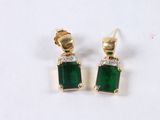 a pair of emerald and diamond earrings on a white surface