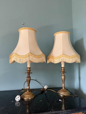 une paire de lampes de table en laiton avec des abat-jours à franges, posées sur une table noire