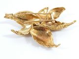 a gold flower brooch with leaves on a white background