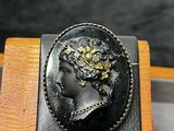 une image représentant une broche noire et dorée orné d'un visage de femme