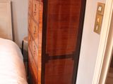 a tall wooden cabinet in the corner of a bedroom
