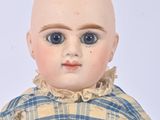a small doll with blue eyes sitting on a white surface