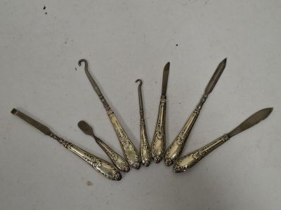 six cuillères et un couteau anciens en argent, posés sur un plateau blanc