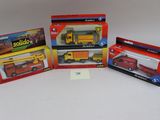On voit trois camions miniatures dans leur boîte posés sur une surface blanche