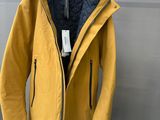 une veste jaune suspendue à un cintre devant un mur gris