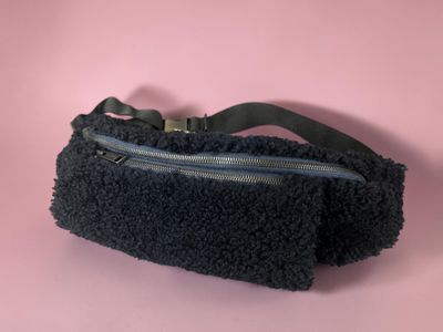 the black purse is on a pink surface with a black strap