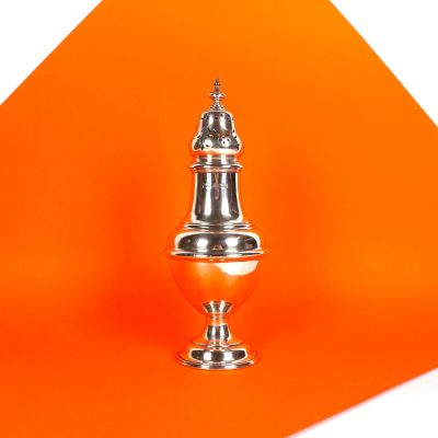un fond orange sur lequel trône un vase argenté