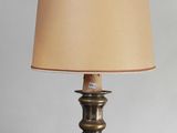 une lampe de table ancienne en laiton, avec un abat-jour beige, posée sur une table en bois