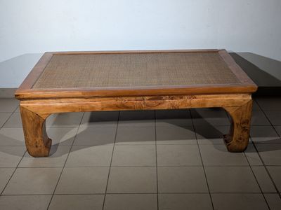 a small wooden table with a woven top on a tiled floor