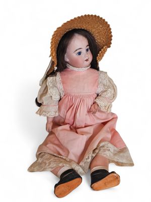 an old doll sitting on the ground wearing a pink dress and a straw hat