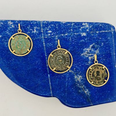 trois pendentifs représentant des pièces de monnaie romaines antiques posés sur une dalle de pierre bleue
