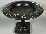 a black plate with flowers and leaves on it on a pedestal