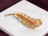 gold plated leaf brooch on a marble surface