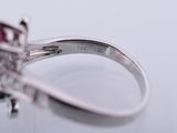 a close up of a diamond and ruby ring on a white surface