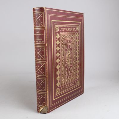 an old red book with gold trim sitting on top of a white surface