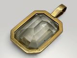 a close up of a gold pendant with a faceted green quartz stone