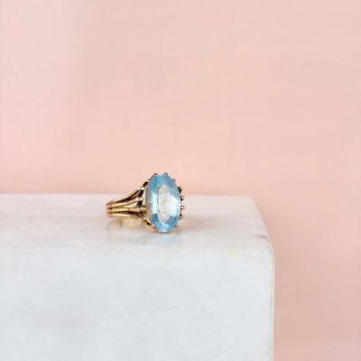 a gold ring with a blue topaz stone on top of a white marble block