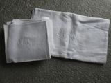 deux serviettes blanches ornées de monogrammes, posées par terre