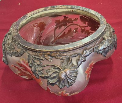 un vase en argent contenant un verre, posé sur un tissu rouge
