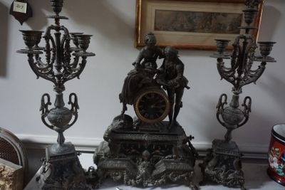 une horloge en argent posée sur une table, à côté de trois chandeliers