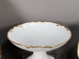a white bowl with gold decoration on it and two vases on a table