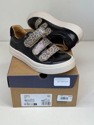 des baskets noires à imprimé léopard, avec des semelles blanches, posées sur une boîte en carton