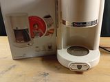 a white coffee maker sitting on a table next to a box