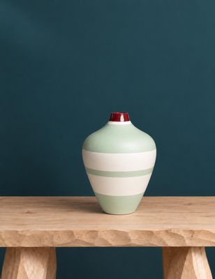 un vase vert posé sur une table en bois, près d'un mur bleu