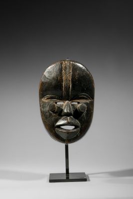 un masque en bois au visage noir, posé sur un socle