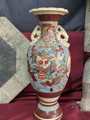 a vase with a painting on it sitting on a red cloth