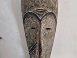 a wooden mask hanging on the wall next to a candle
