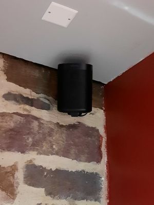 une enceinte noire posée sur un mur de briques dans un coin de la pièce