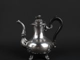 an antique silver teapot on a stand against a black background