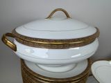 a white bowl with gold trim and a gold rim on top of a stack of plates