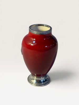 a red vase with a silver lid sitting on a white surface