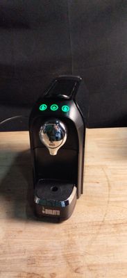 a black coffee maker on a wooden table next to a cup