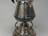 a silver tea pot with a black handle on a stand