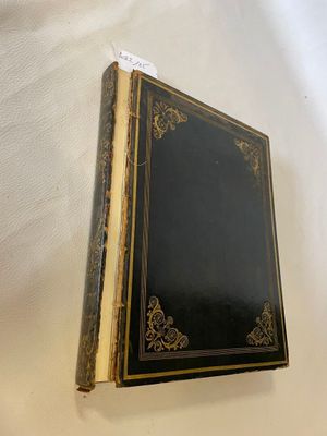 an old book with a black cover sitting on top of a table