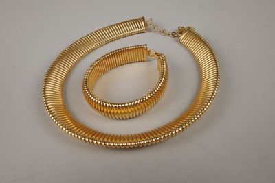 un gros plan d'un collier et d'un bracelet en or posés sur une surface blanche