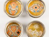 quatre petits boutons métalliques arborant différents motifs sur un fond blanc