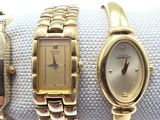 three gold watches are sitting on a white cloth on a white surface