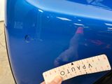 a person holding a ruler in front of a blue car