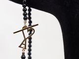 a close up of a black beaded bracelet with a gold letter on it
