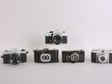 four old cameras are lined up on a white surface